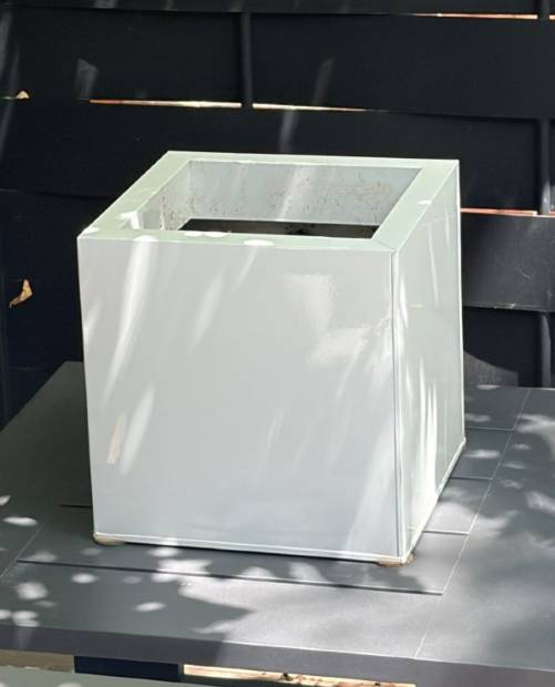An empty white cube planter against a dark fence
